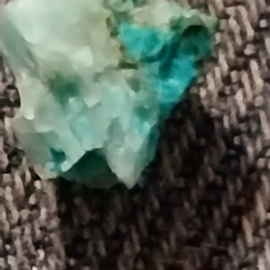 May include: A close-up of a turquoise and green gemstone with a rough, irregular shape.