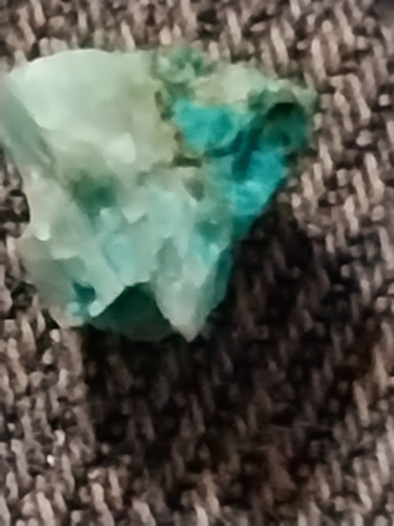May include: A close-up of a turquoise and green gemstone with a rough, irregular shape.