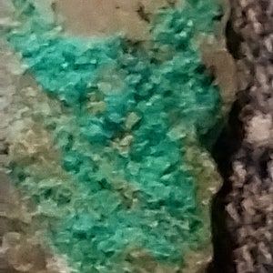 May include: A close-up of a rock with a green mineral deposit. The mineral has a rough, crystalline texture.