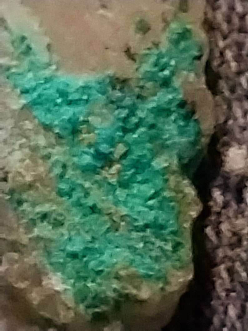 May include: A close-up of a rock with a green mineral deposit. The mineral has a rough, crystalline texture.