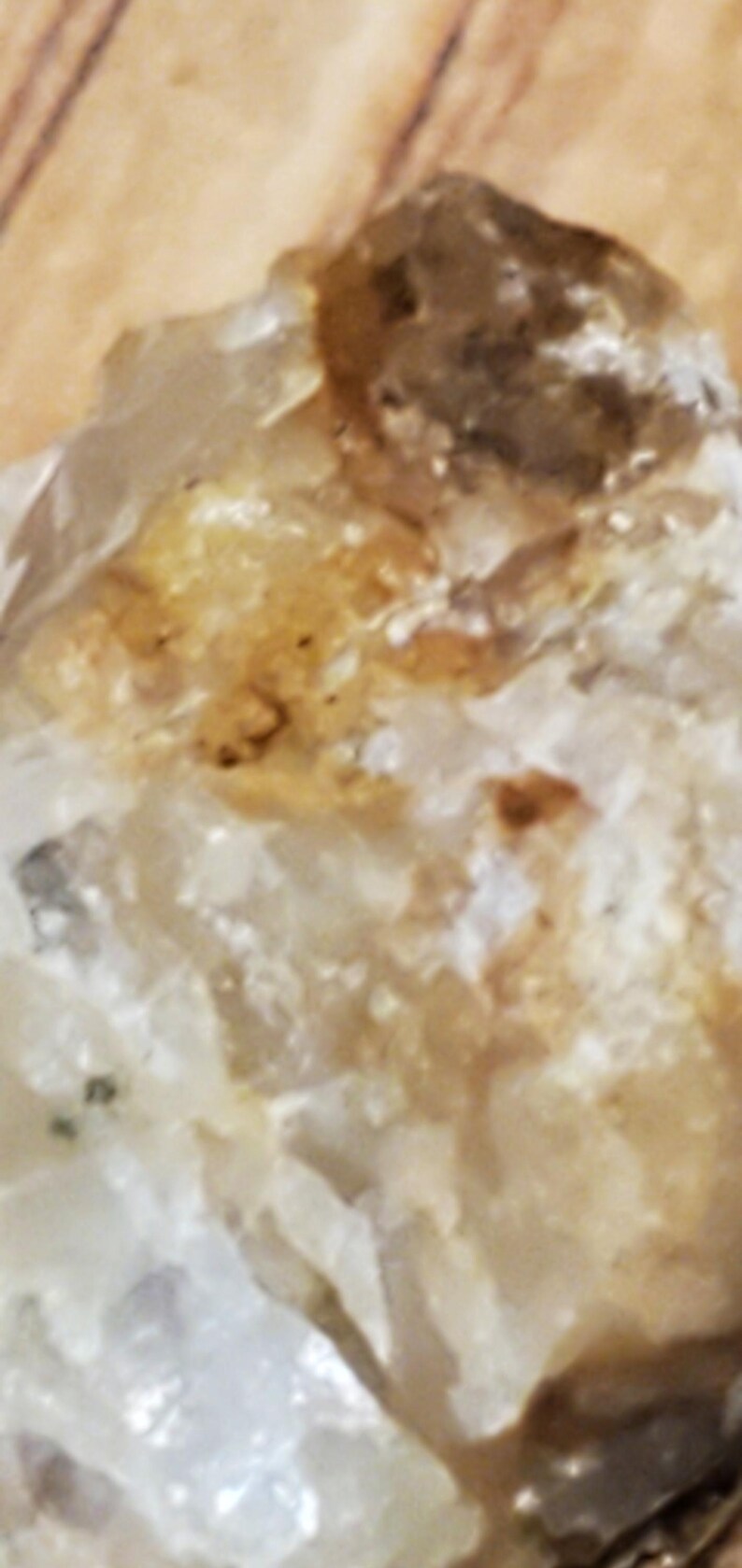 May include: Close-up of a raw, natural quartz crystal. The crystal has a translucent, milky white base with areas of light brown and amber coloration. The surface has a rough, textured appearance.