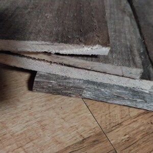 May include: Close-up of weathered, gray wooden planks stacked on top of each other. The wood has a rough texture with visible grain and a natural, aged appearance. The planks are of varying lengths and widths.
