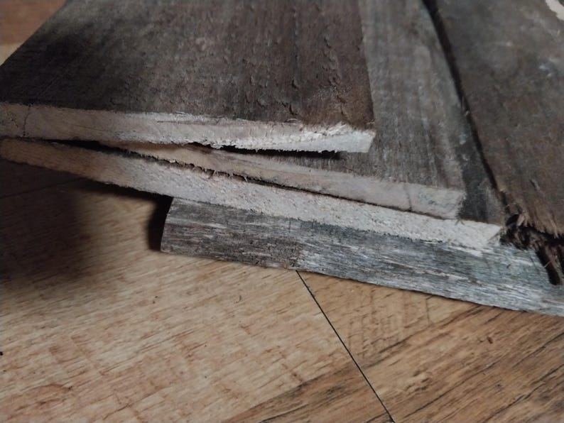 May include: Close-up of weathered, gray wooden planks stacked on top of each other. The wood has a rough texture with visible grain and a natural, aged appearance. The planks are of varying lengths and widths.