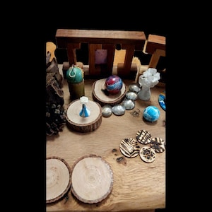 May include: A collection of decorative items on a wooden surface. Includes small wooden coasters with leaf designs, a blue and white figurine, a colorful sphere, and various polished stones. The items are arranged on wooden slices and a wooden structure.