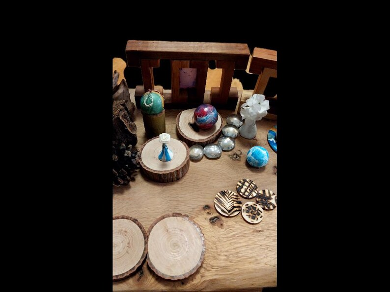 May include: A collection of decorative items on a wooden surface. Includes small wooden coasters with leaf designs, a blue and white figurine, a colorful sphere, and various polished stones. The items are arranged on wooden slices and a wooden structure.