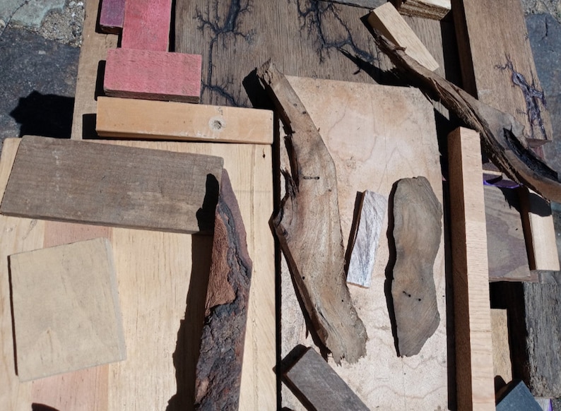 May include: A collection of wood pieces in various shapes, sizes, and colors. Some pieces are smooth and polished, while others are rough and textured. The wood pieces are arranged in a random pattern on a wooden surface.