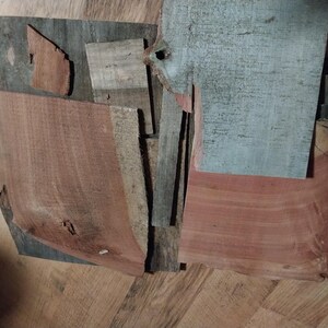May include: An assortment of irregularly shaped wood pieces in various shades of brown, gray, and red. The pieces have visible grain patterns and textures, suggesting they are reclaimed or repurposed. The arrangement is abstract and artistic.