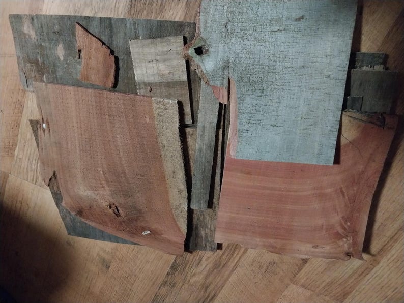 May include: An assortment of irregularly shaped wood pieces in various shades of brown, gray, and red. The pieces have visible grain patterns and textures, suggesting they are reclaimed or repurposed. The arrangement is abstract and artistic.