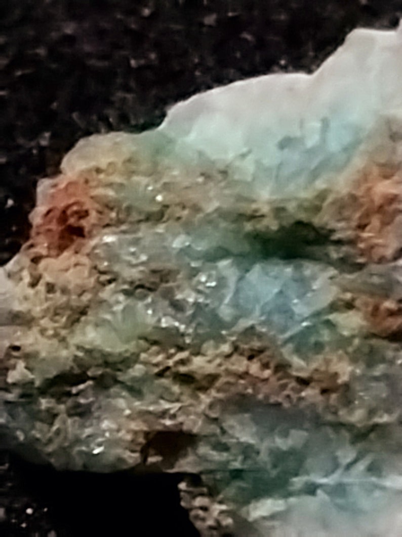 May include: A close-up of a rough, layered rock with a mix of green, brown, and white colors. The rock has a crystalline texture and appears to be a natural mineral specimen.