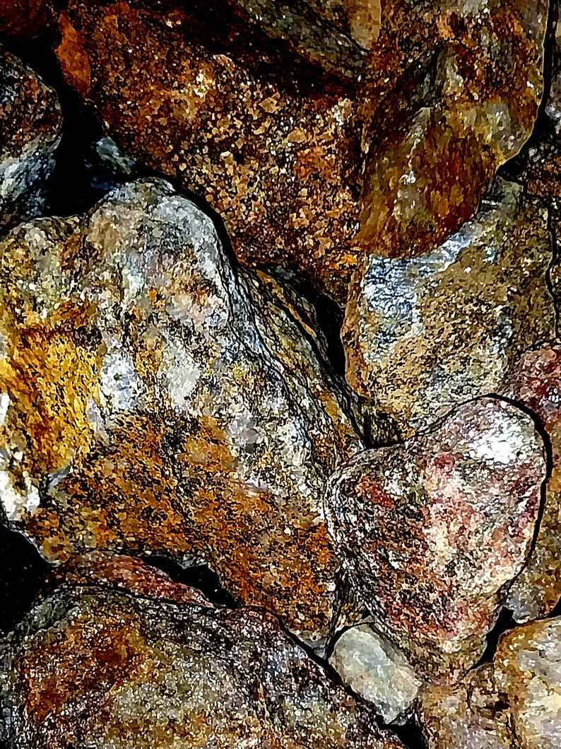 May include: Close-up of a collection of various rocks. The rocks display a mix of colors, including shades of brown, gold, gray, and hints of red. The textures vary, with some appearing smooth and others rough and granular.