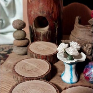 May include: A rustic display featuring wooden coasters, a stacked stone sculpture, and a decorative wooden birdhouse. A small vase with white flowers and a decorative wooden piece are also present. The items are arranged on a wooden surface.