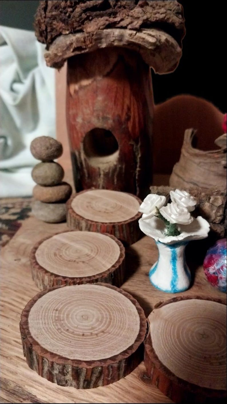 May include: A rustic display featuring wooden coasters, a stacked stone sculpture, and a decorative wooden birdhouse. A small vase with white flowers and a decorative wooden piece are also present. The items are arranged on a wooden surface.