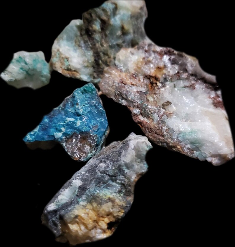 May include: A collection of rough, raw mineral specimens. The stones are a mix of white, blue, green, and brown.