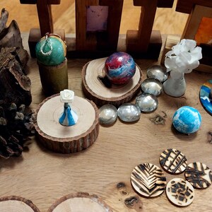May include: A collection of decorative objects, including wooden sculptures, painted spheres, and small, round wooden coasters. The items are arranged on a wooden surface, showcasing a variety of colors and textures. The scene is well-lit, highlighting the details of each piece.