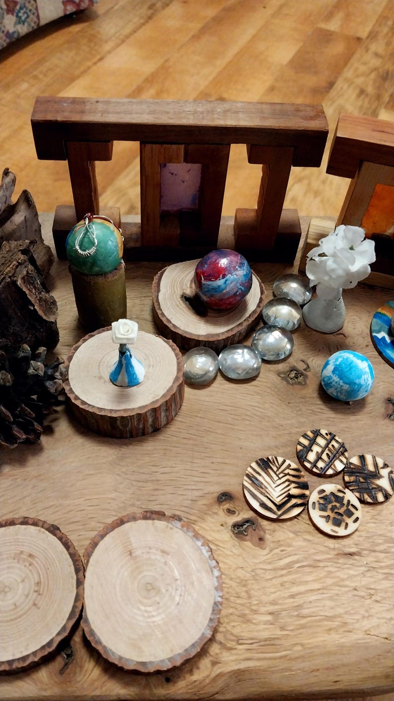 May include: A collection of decorative objects, including wooden sculptures, painted spheres, and small, round wooden coasters. The items are arranged on a wooden surface, showcasing a variety of colors and textures. The scene is well-lit, highlighting the details of each piece.