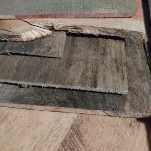 May include: A collection of weathered, reclaimed wood planks in varying sizes and shades of gray and brown. Some planks have visible grain and texture, with rough edges and signs of wear. The wood appears to be repurposed.