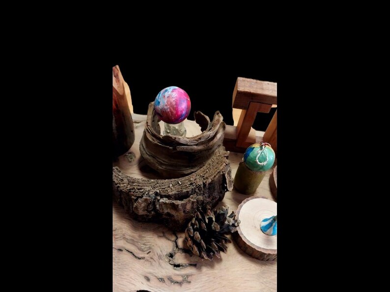 May include: A collection of decorative spheres and wooden elements. A colorful sphere with pink, blue, and purple hues sits atop a wooden base. Other spheres with green and blue accents are displayed on wooden stands. The scene is set on a wooden surface.