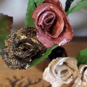 May include: Three artificial roses with glitter. The roses are in shades of gold, copper, and cream.