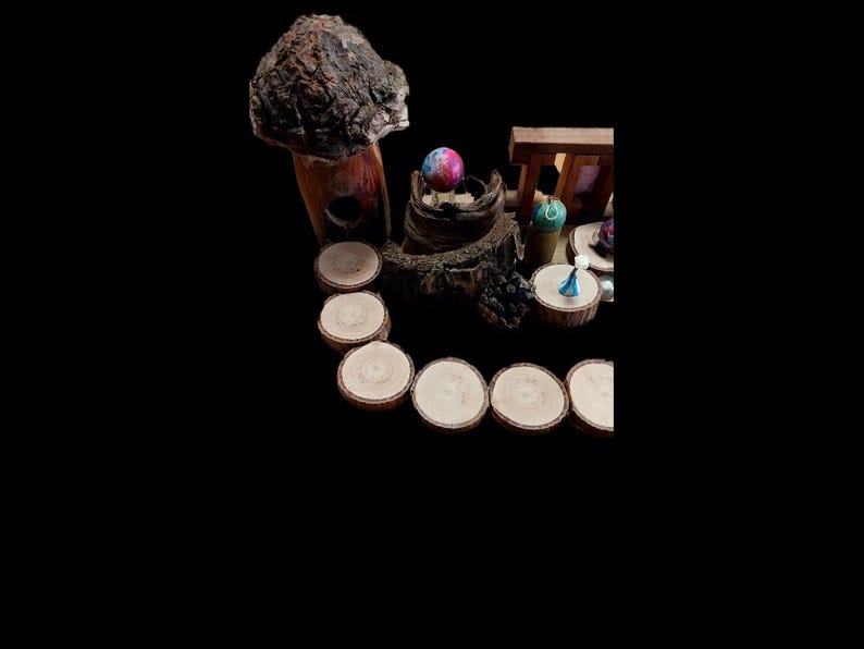 May include: A whimsical arrangement featuring a large, textured mushroom, a colorful sphere, and miniature figurines. Wooden slices are arranged in a semi-circle. The scene is set against a black background, creating a dramatic contrast.