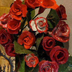 May include: A bouquet of red and white roses made of paper or fabric. The roses are arranged in a circular shape and have a glossy finish.