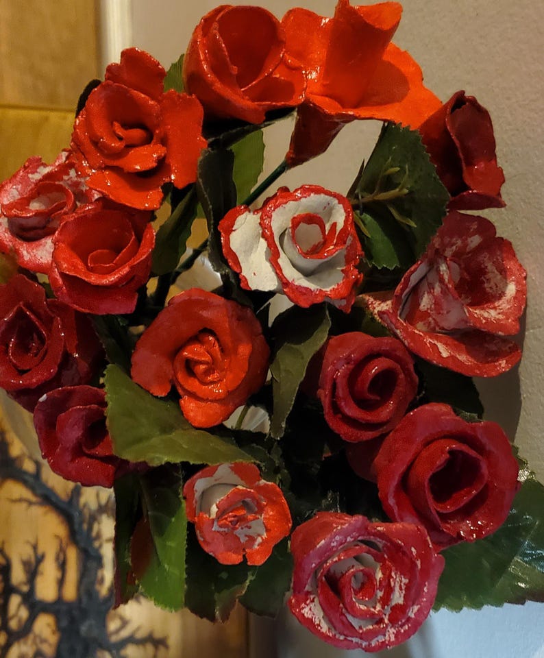 May include: A bouquet of red and white roses made of paper or fabric. The roses are arranged in a circular shape and have a glossy finish.