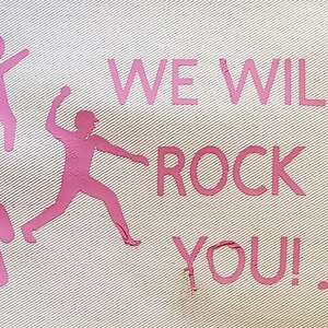 May include: Off-white fabric with pink text and graphics. The text reads "WE WILL ROCK YOU!" with three stylized figures throwing objects. A pink cloud-like shape is also present.