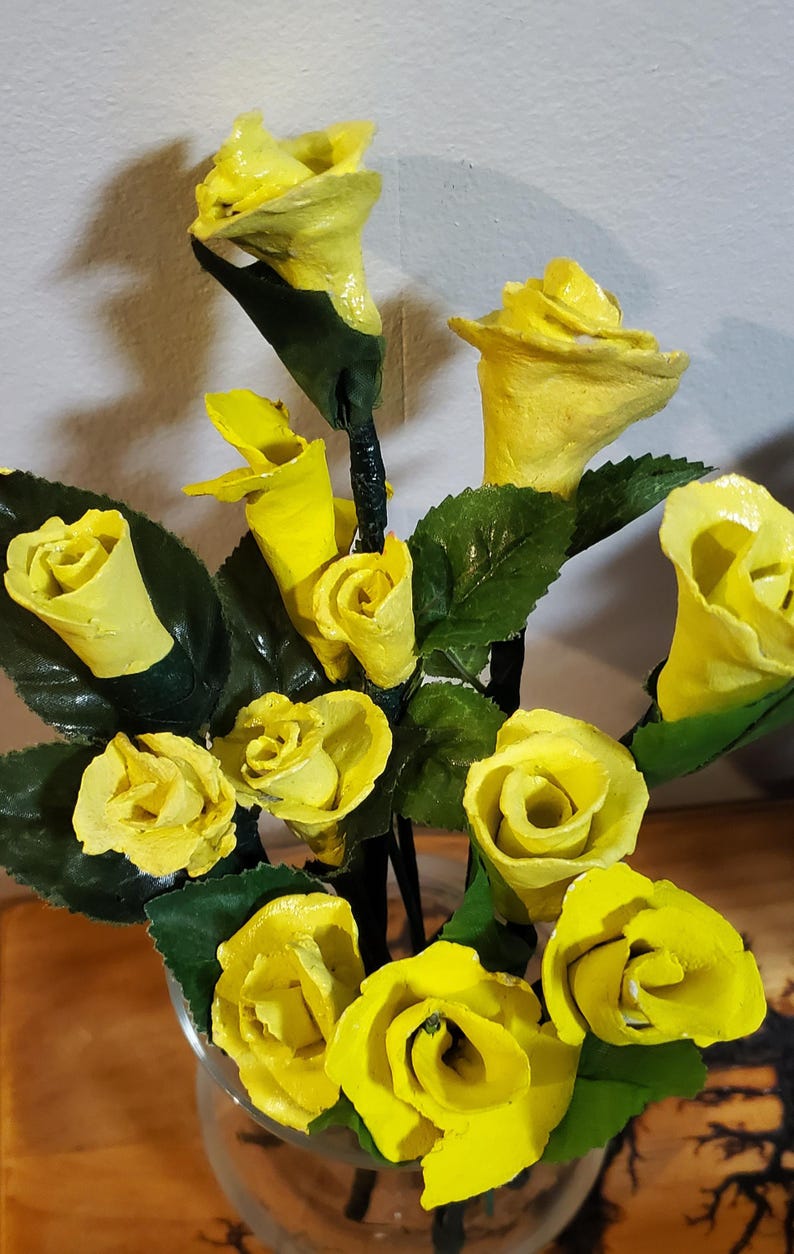 May include: A bouquet of yellow paper roses in a clear glass vase. The roses are made of paper and have a realistic appearance.