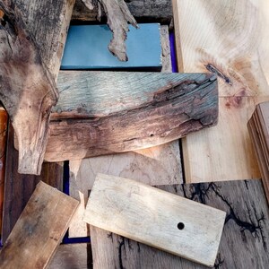 May include: A collection of wood pieces, including a piece of driftwood, a piece of wood with a hole drilled in it, and a piece of wood with a blue painted surface.
