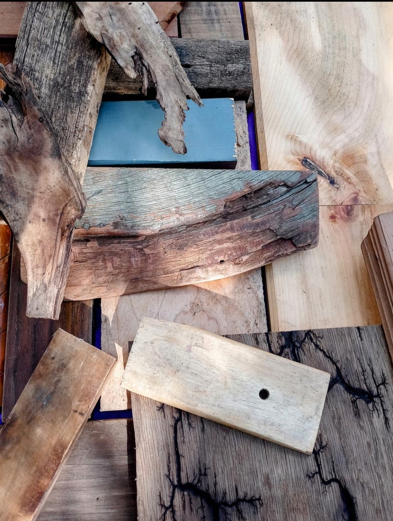 May include: A collection of wood pieces, including a piece of driftwood, a piece of wood with a hole drilled in it, and a piece of wood with a blue painted surface.