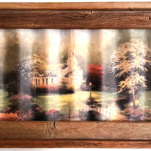 May include: A rustic wooden framed art print featuring a serene landscape with a church, bridge, and trees. The artwork has a vintage aesthetic, with soft colors and a textured appearance. The frame is made of weathered wood.
