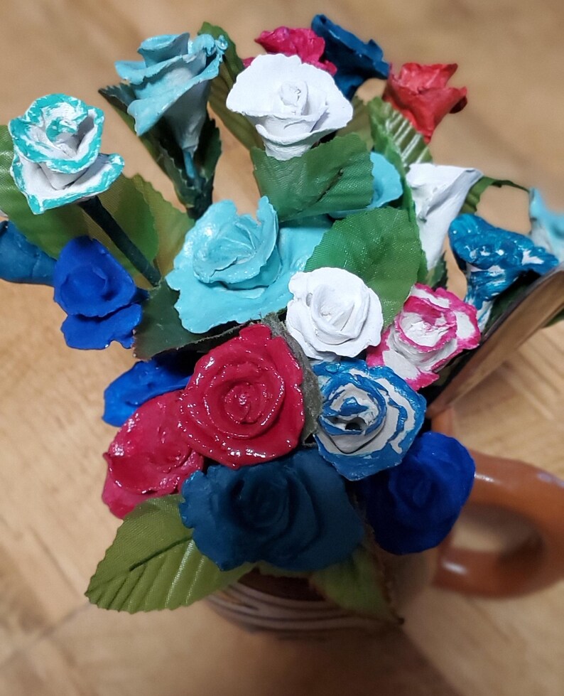 May include: A bouquet of paper flowers in a brown ceramic vase. The flowers are painted in shades of blue, red and white.