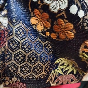 May include: Close-up of a dark blue fabric with an intricate floral and geometric pattern. The design features orange, white, and gold flowers, along with detailed hexagonal shapes. The fabric has a textured appearance.
