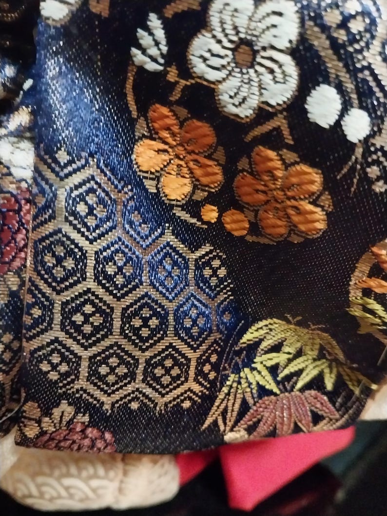 May include: Close-up of a dark blue fabric with an intricate floral and geometric pattern. The design features orange, white, and gold flowers, along with detailed hexagonal shapes. The fabric has a textured appearance.