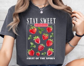 May include: A gray t-shirt with the text "Stay Sweet" and "Fruit of the Spirit" with a graphic of strawberries and leaves. The text "Galatians 5:22-23" is also included.