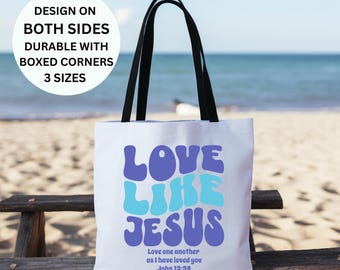 May include: White tote bag with black handles featuring a blue and purple graphic that says "Love Like Jesus" with the scripture "Love one another as I have loved you John 13:34" printed below.