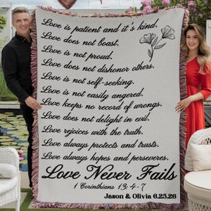 May include: A woven throw blanket with the text "Love is patient and it's kind" and other related phrases. The blanket has a cream background with black text and a floral design. The bottom of the blanket has the text "Love Never Fails" and the names "Jason & Olivia 6.25.26".