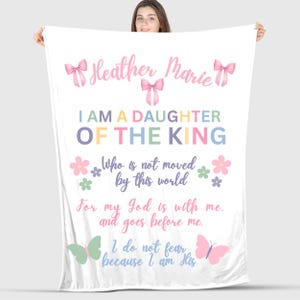 May include: White blanket with the text "Heather Marie I AM A DAUGHTER OF THE KING" in various colors. The blanket features pink bows, flowers, and butterflies. The blanket also has the text "Who is not moved by this world" and "For my God is with me, and goes before me. I do not fear because I am His."