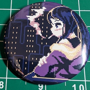 May include: A round button with a pixelated illustration of a person with dark hair and a purple outfit, set against a cityscape background. The design features shades of purple, white, and black.