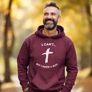 Op de afbeelding: Bordeauxkleurige hoodie met een wit kruis en de tekst "Ik kan niet... maar ik ken iemand!"