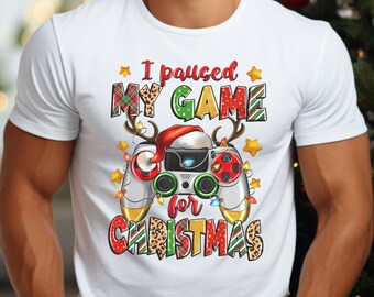 Könnte beinhalten: Weißes T-Shirt mit einem Weihnachtsmotiv. Das Design zeigt einen Videospiel-Controller mit einer Weihnachtsmütze und dem Text "Ich habe mein Spiel für Weihnachten pausiert".