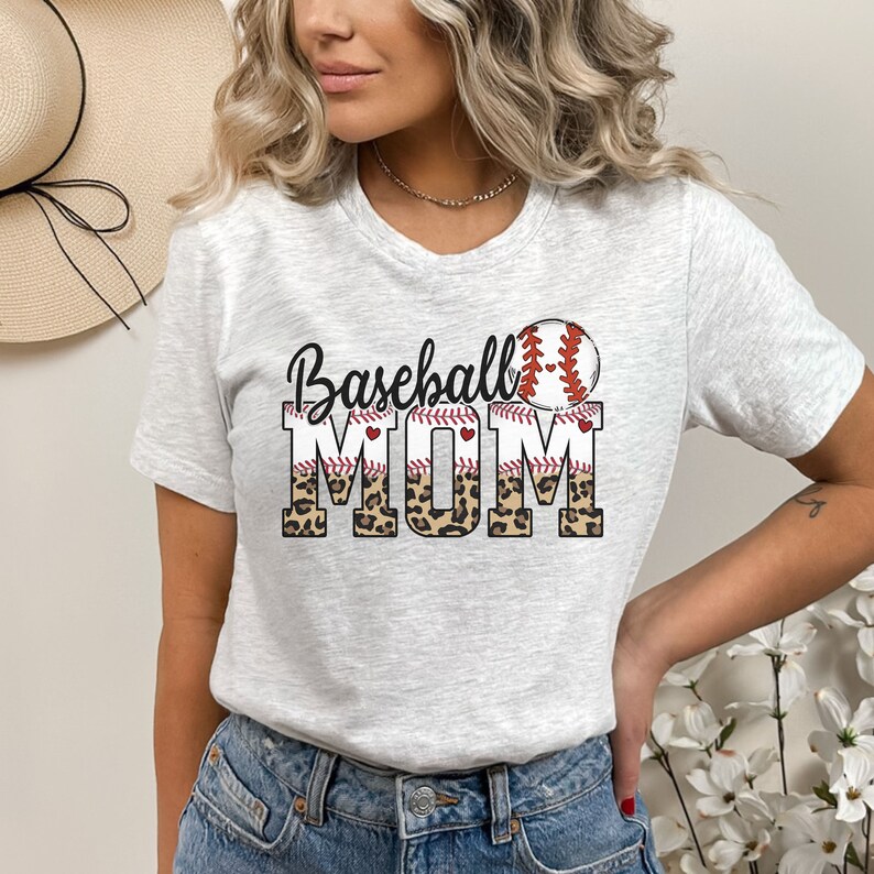 May include: A white t-shirt with a graphic design that says "Baseball Mom" in black text with a red baseball and red stitching. The word "Mom" is in a leopard print pattern.