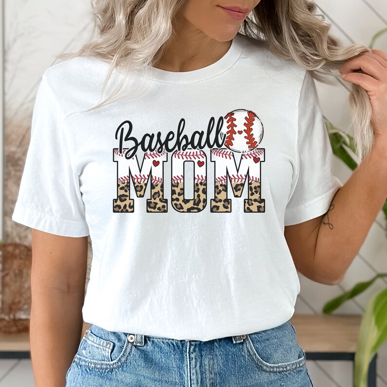 May include: White t-shirt with the text "Baseball Mom" in black with a red baseball stitch design and a baseball graphic. The text "Mom" is in a leopard print pattern.