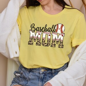 May include: Yellow t-shirt with the text "Baseball Mom" in black and red lettering with a baseball graphic and leopard print accents.