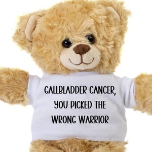May include: A tan teddy bear wearing a white t-shirt with the text "Gallbladder Cancer, You Picked The Wrong Warrior" in black. The bear has a smiling face and is set against a white background.