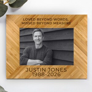 May include: A rectangular bamboo photo frame with a chevron pattern. The top border is engraved with the text LOVED BEYOND WORDS, MISSED BEYOND MEASURE. The bottom border is engraved with the text JUSTIN JONES 1988-2026. A black and white photo is inside.