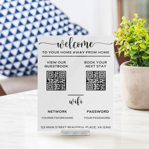 May include: White sign with black text that says "welcome to your home away from home".  The sign also includes two QR codes, one labelled "view our guestbook" and the other labelled "book your next stay".  The sign also includes the word "wifi" and the text "network yournetworkname" and "password your password".  The sign also includes the address "123 Main Street Beautiful Place, VA 12345".