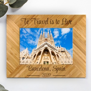 May include: A rectangular bamboo picture frame with a light brown wood grain. The top border is engraved with the text "To Travel is to Live" and the bottom border features "Barcelona, Spain" above the year "2020". A photo of the Sagrada Familia is inside.