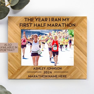 May include: A wooden photo frame with a runner in a red shirt and a woman in a black tank top running in a race. The frame has the text "The year I ran my first half marathon" and "Ashley Johnson 2024 Marathon name here".