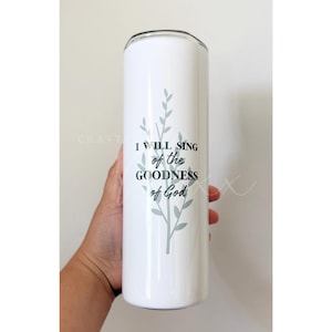 May include: White stainless steel tumbler with a black lid. The tumbler features a light green floral design and the text "I WILL SING of the GOODNESS of God" in black. The tumbler is held by a person.