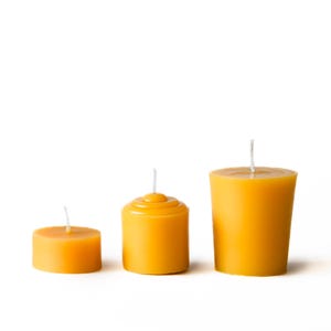 Puede incluir: Tres velas amarillas de diferentes formas y tamaños dispuestas sobre un fondo blanco. Las velas tienen mechas blancas y un color liso y uniforme. Las velas son cilíndricas y redondas, ideales para la decoración del hogar.